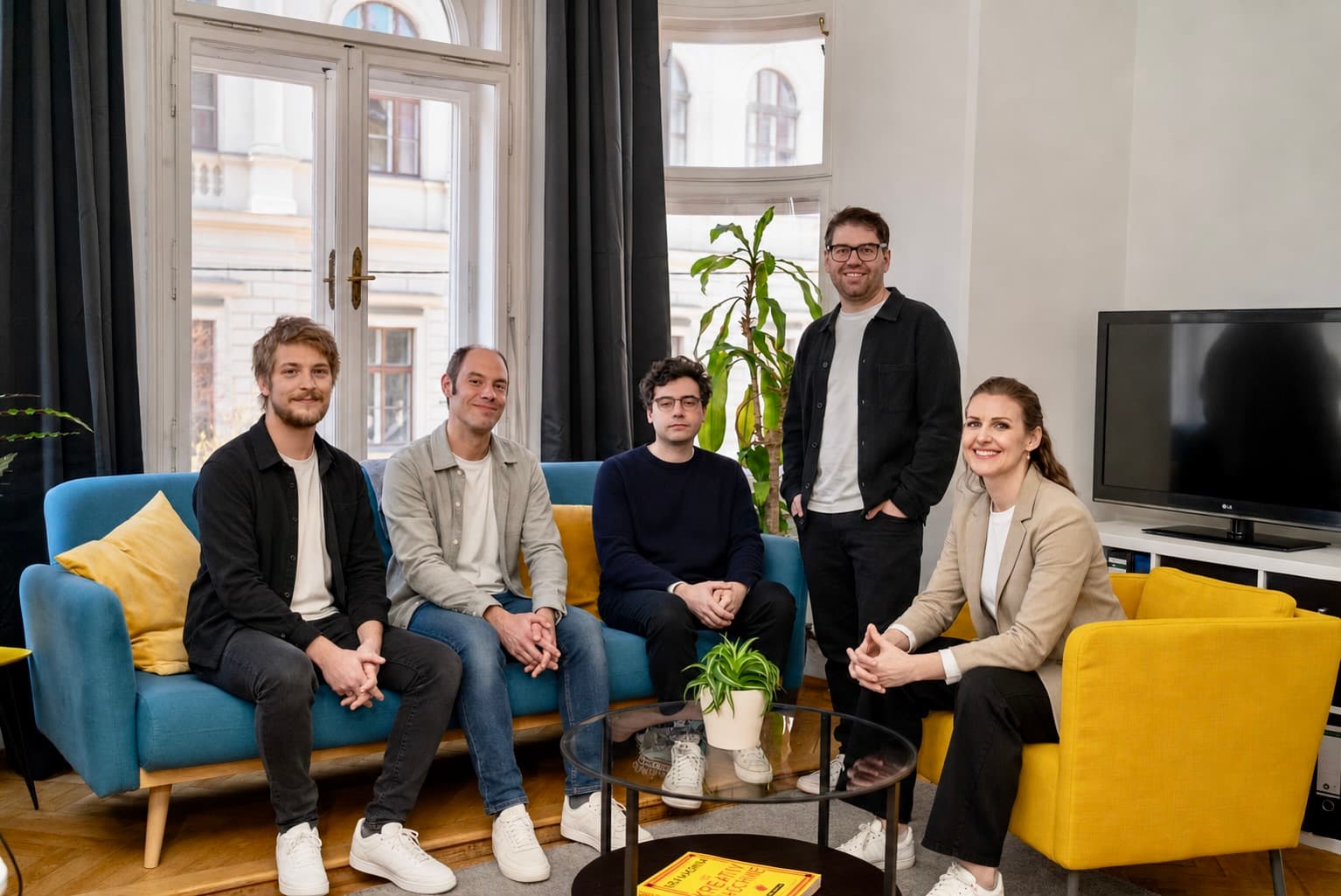 Fröhliche Projektbesprechung am Computer um einen runden Glastisch.